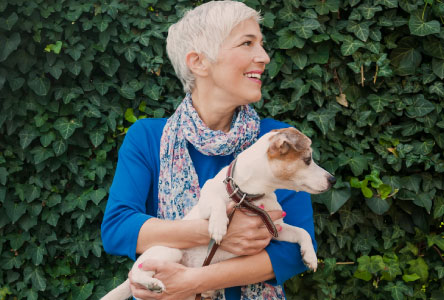 Middle-aged woman holding a small dog and smiling.