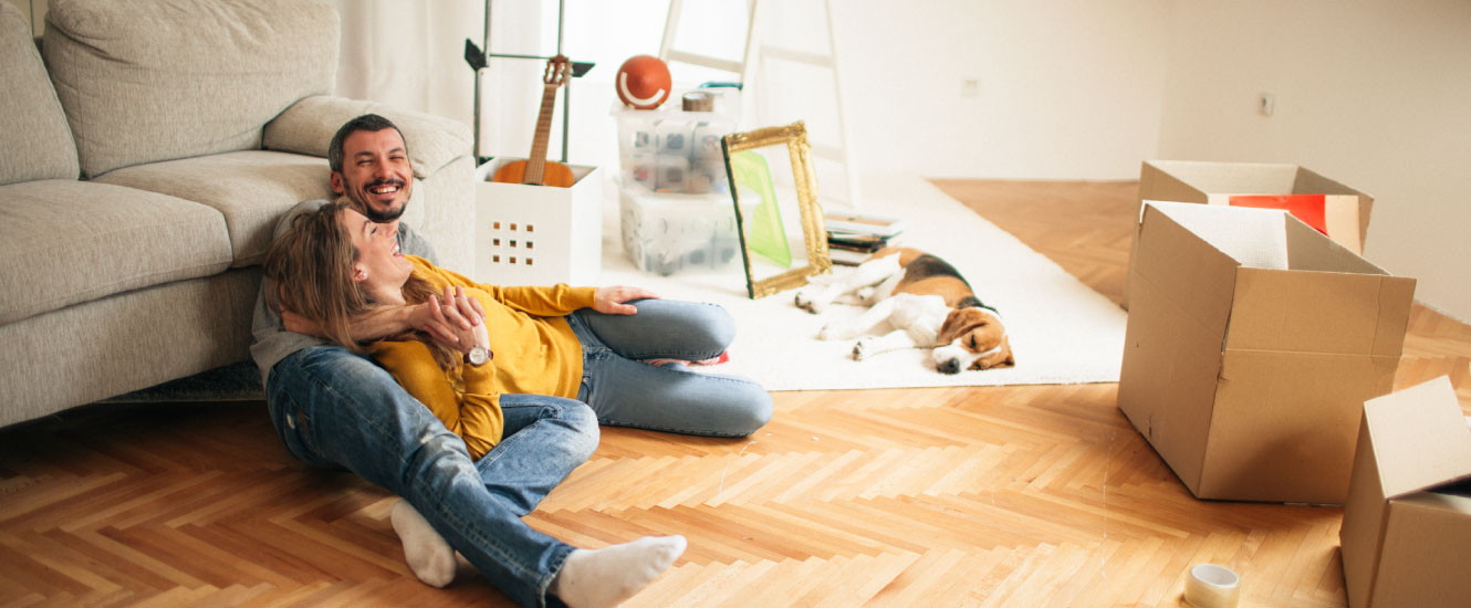 A young couple sitting on the floor of a large empty room with cardboard moving boxes.