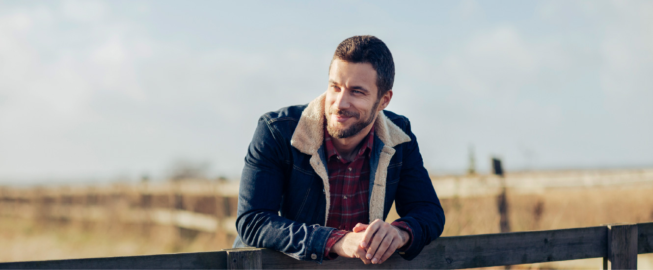 A young man leaning against a wooden fence, smiling.