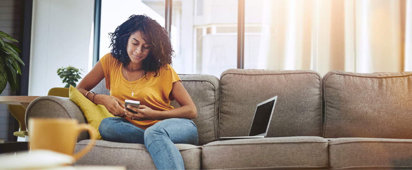 Young woman sitting at the end of a long couch looking down at her smartphone.