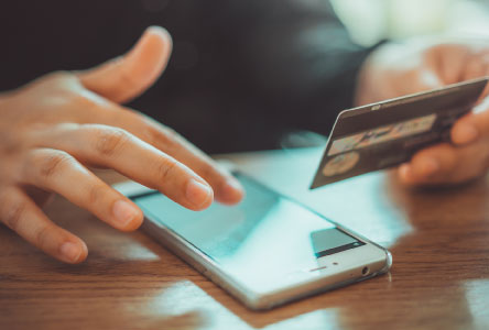 Close up of a person's hand using a smartphone and holding a credit card.