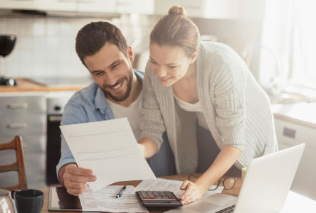 A couple in a kitchen looking over paper documents at a table.