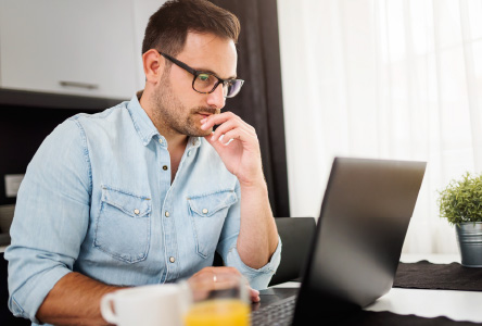 A man sitting at a desk looking down towards a laptop screen.