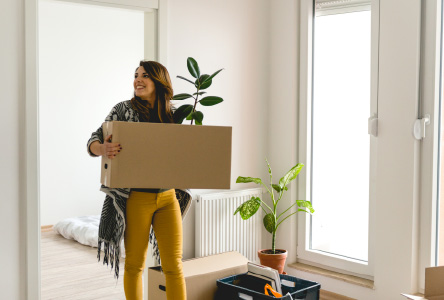 Young woman holding a large cardboard in an empty room.